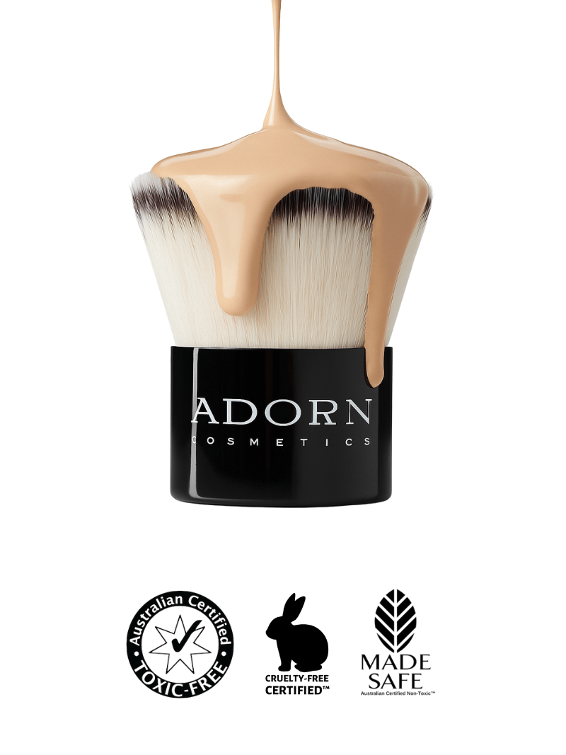 Vegan kabuki foundation brush with foundation liquid, Adorn Cosmetics branding, and certification logos on a white background