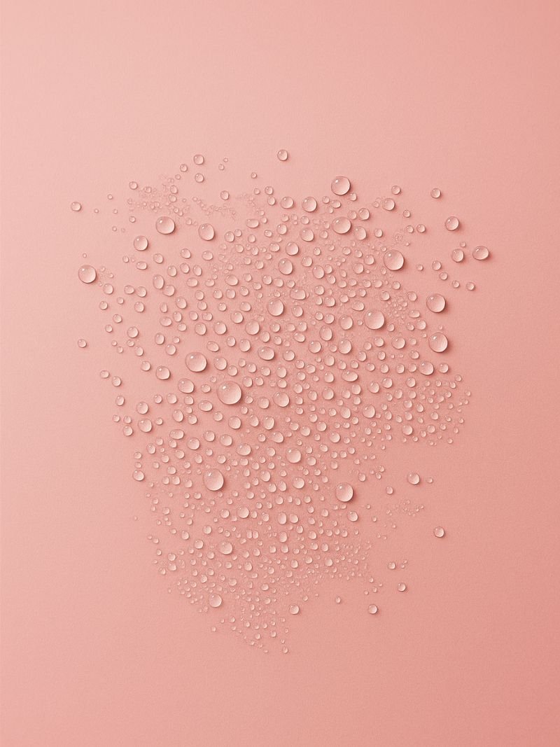 Hydrating rose water mist droplets on a pink surface.