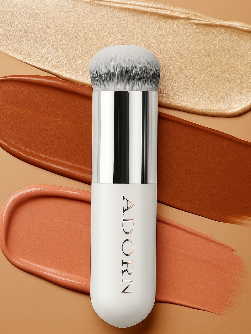 Cream makeup brush with 'ADORN' branding on a beige background with cream mineral makeup swatches.