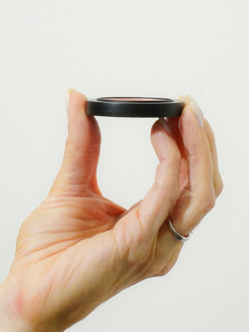 A hand holding Magnetic Stack Middle Section part for Mineral makeup compact stacks on a beige background.