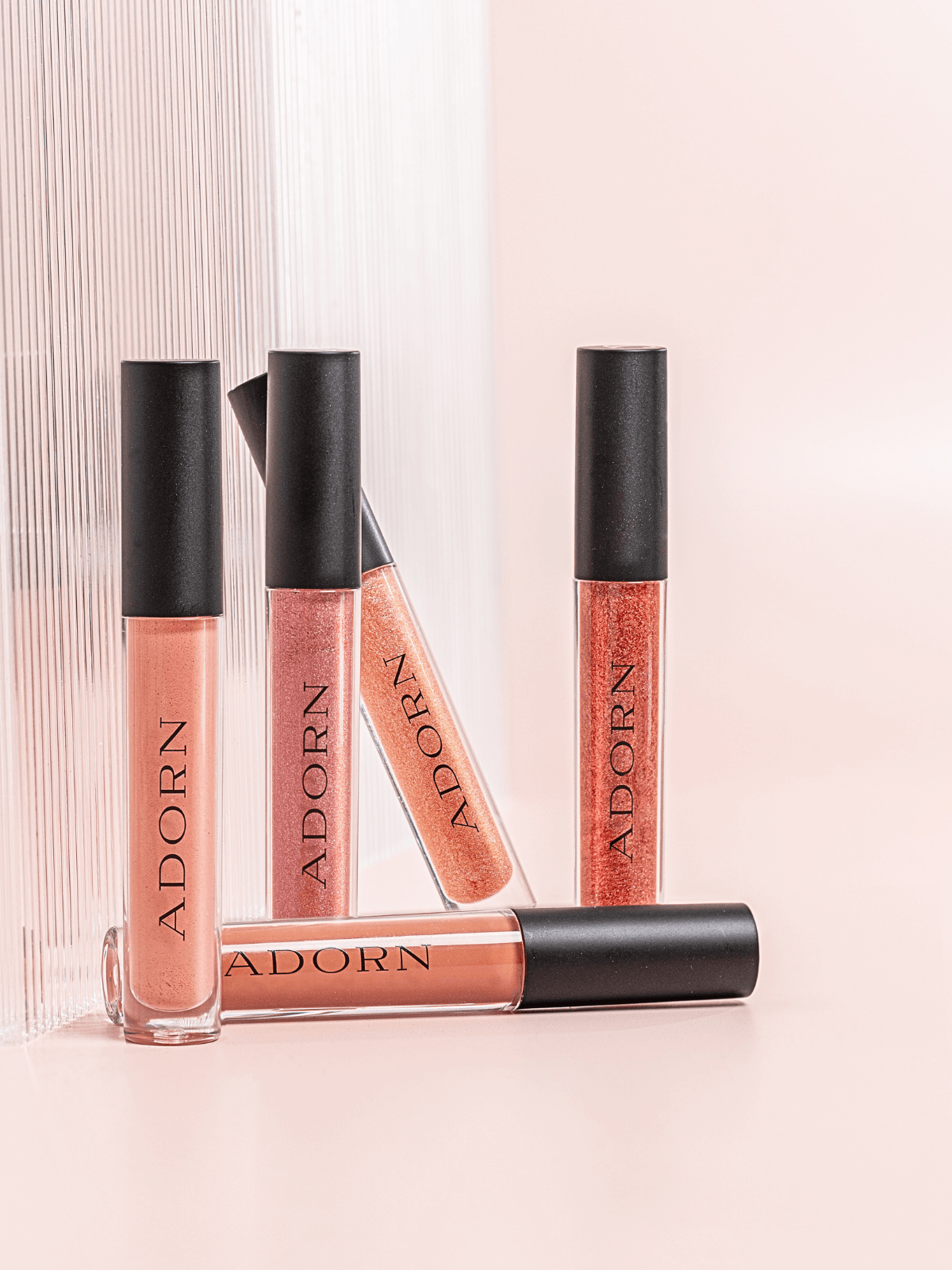 Lip glosses with 'ADORN' branding on a light pink background