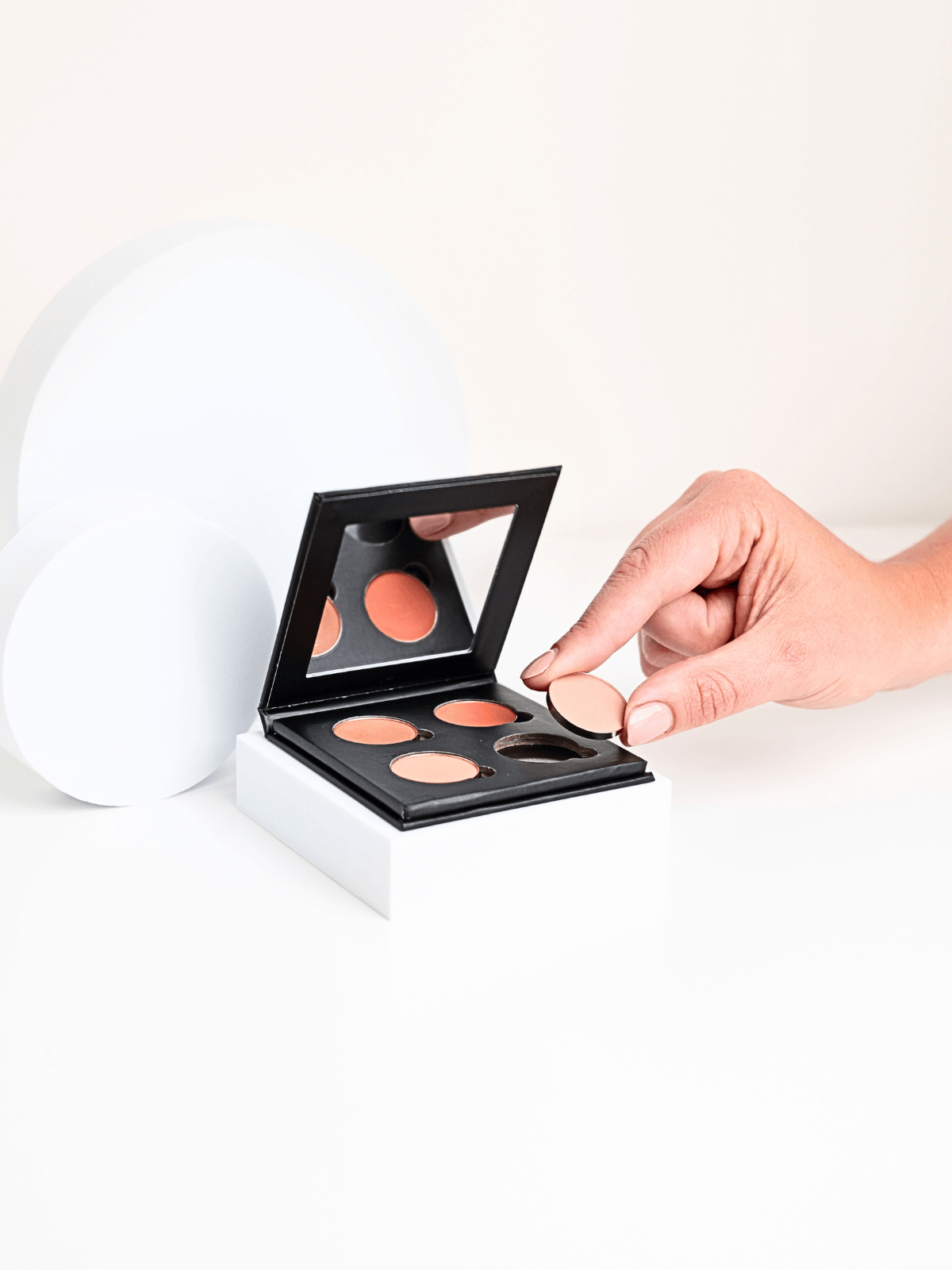 Hand holding a makeup palette with various shades on a white background