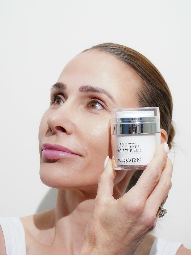 Mature woman holding makeup primer for mature skin jar next to her face on a beige background.