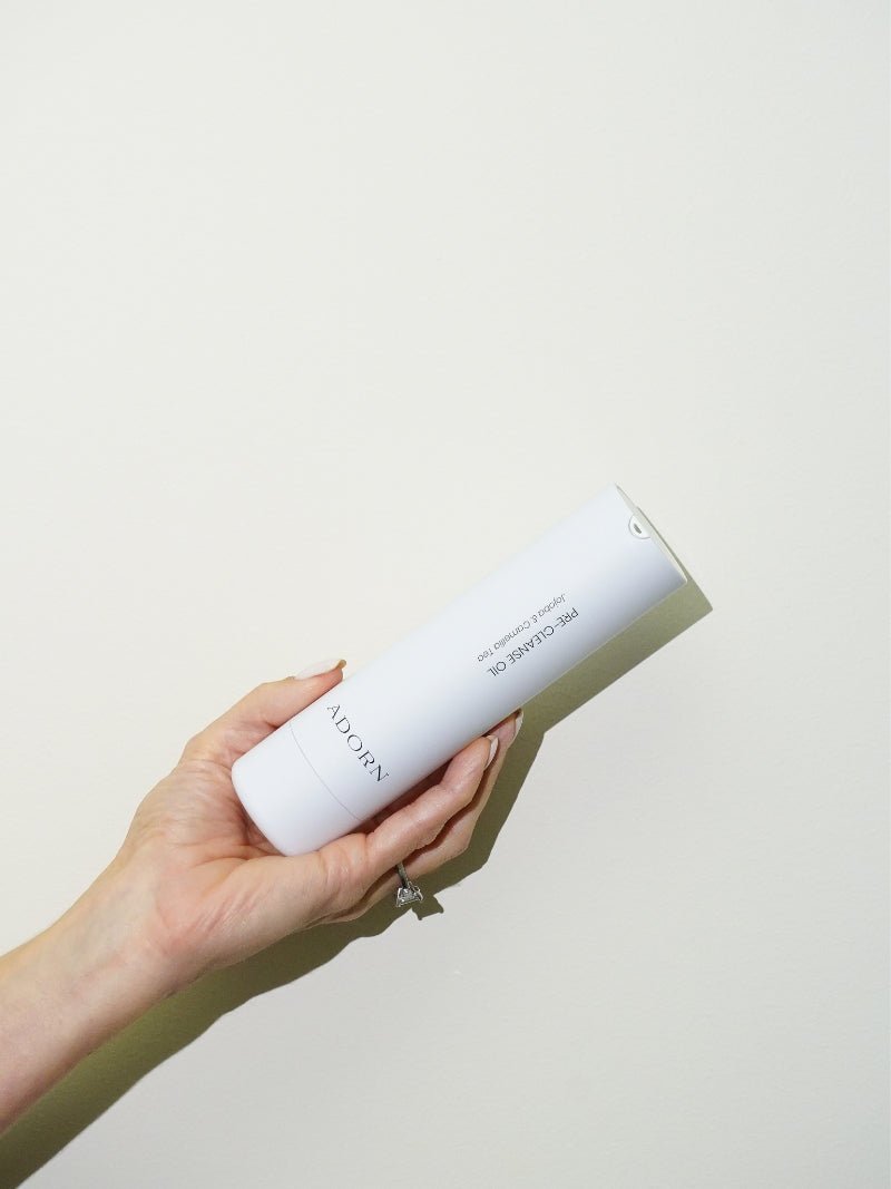 Makeup removing oil bottle in woman's hand, against a beige background.