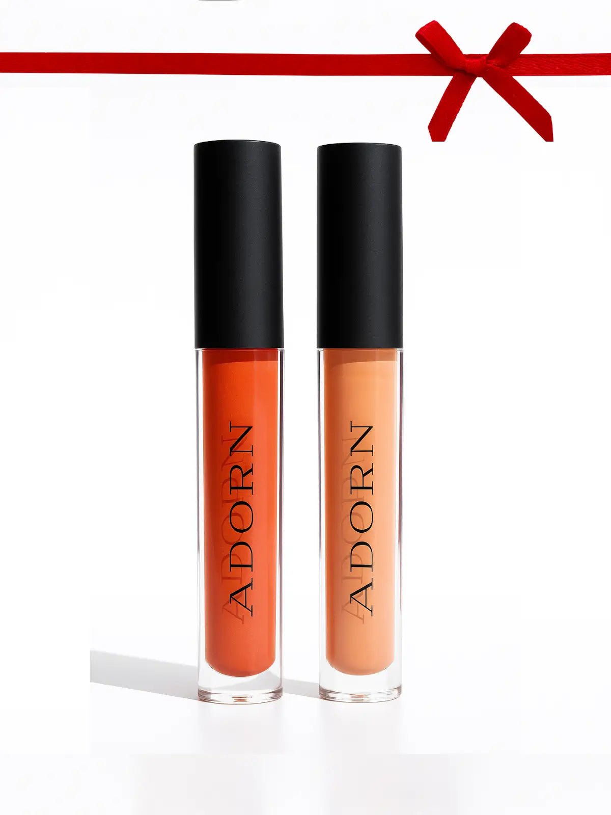 Two lip glosses with black caps labeled 'Adorn' on a white background.