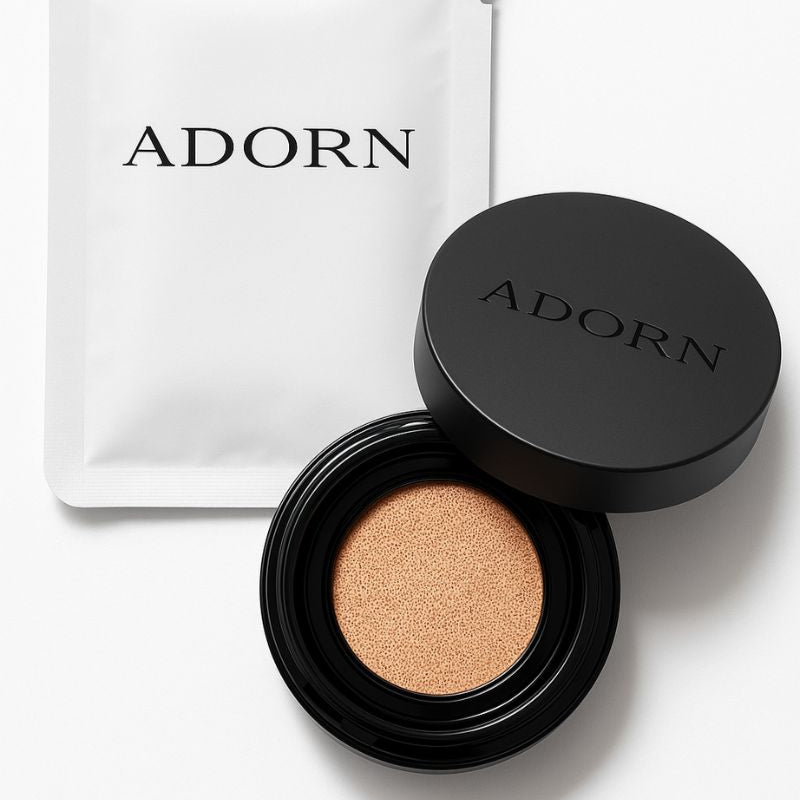 Open cosmetic compact with beige powder and closed black lid on a white background, featuring the brand 'ADORN'.