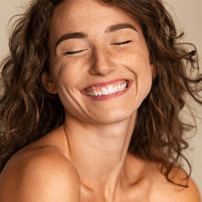 Woman with closed eyes smiling against a neutral background