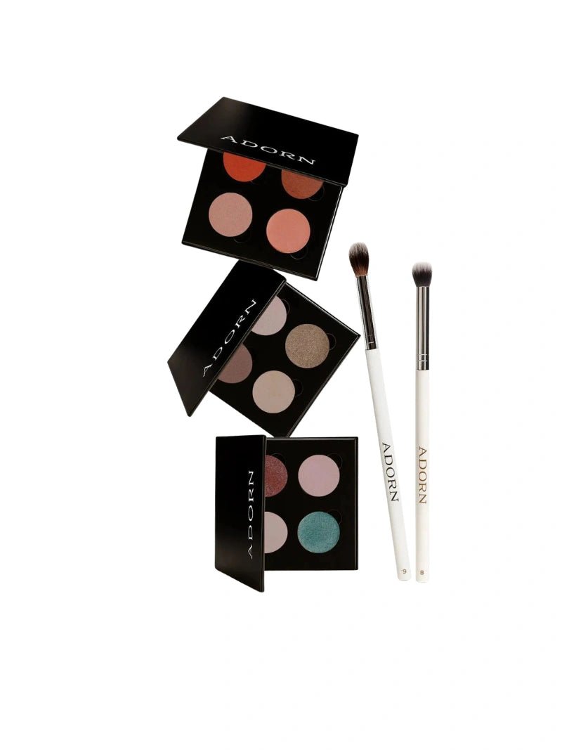 Makeup product set with three eyeshadow palettes and two brushes on a white background, branded 'Adorn'.