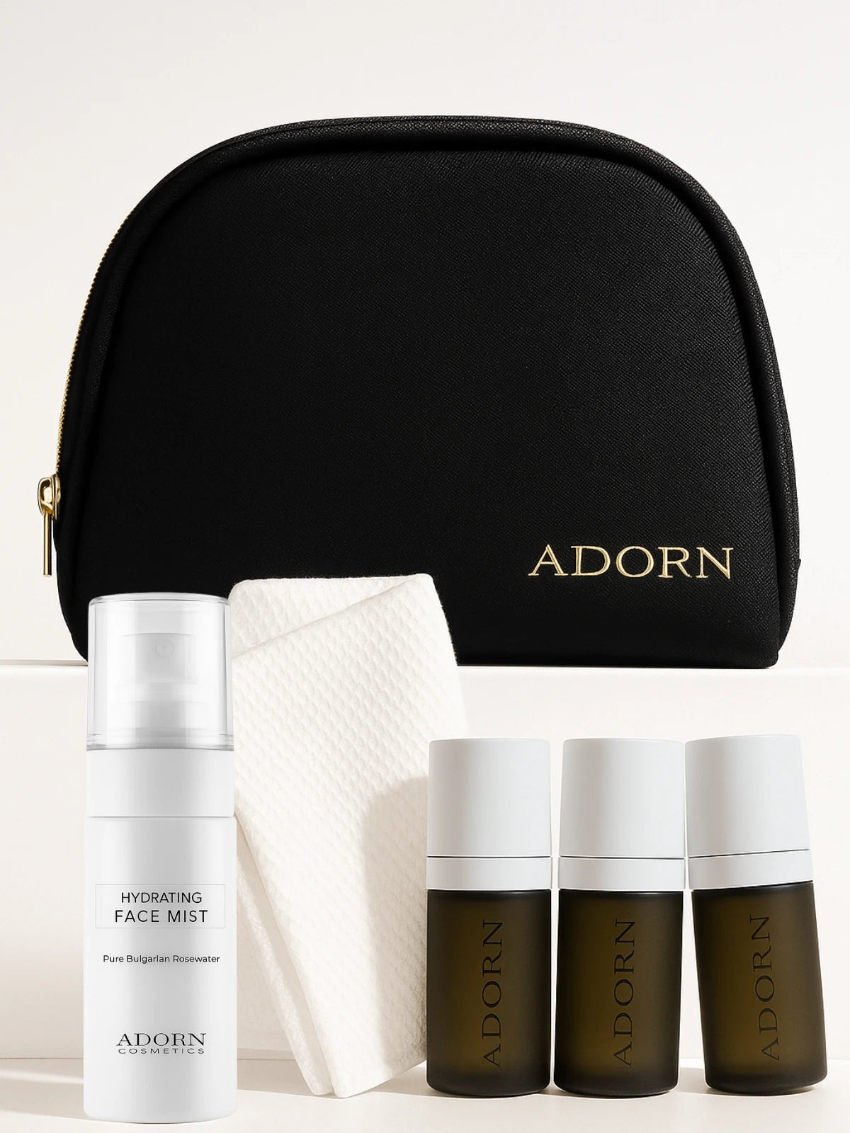 Cosmetic set with 'ADORN' branding including a black pouch, face mist, and skincare bottles on a light background.