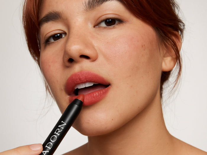 A woman applying Adorn red lipstick