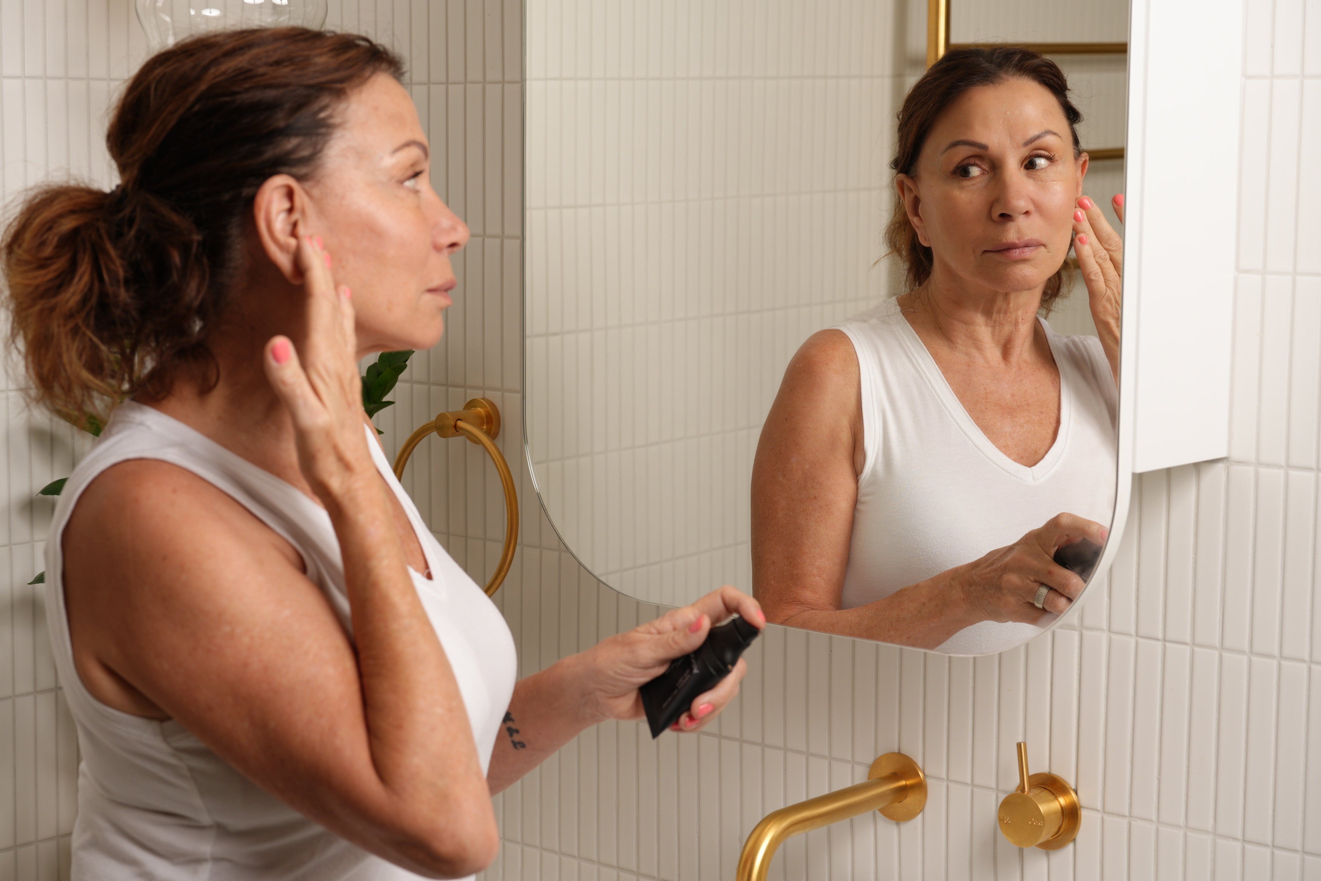 Woman applying mineral makeup in bathroom mirror.