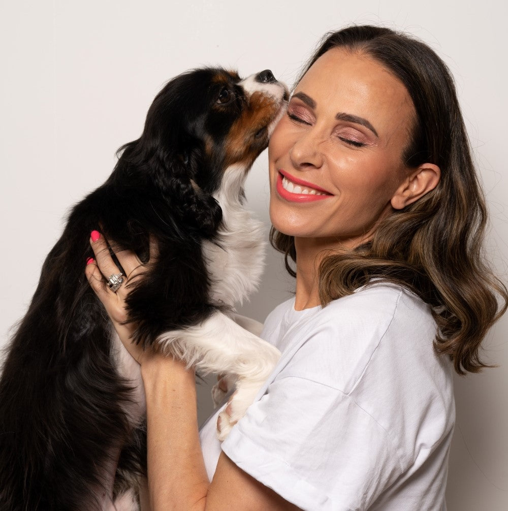Woman holding a Cavalier King Charles Spaniel against a plain background