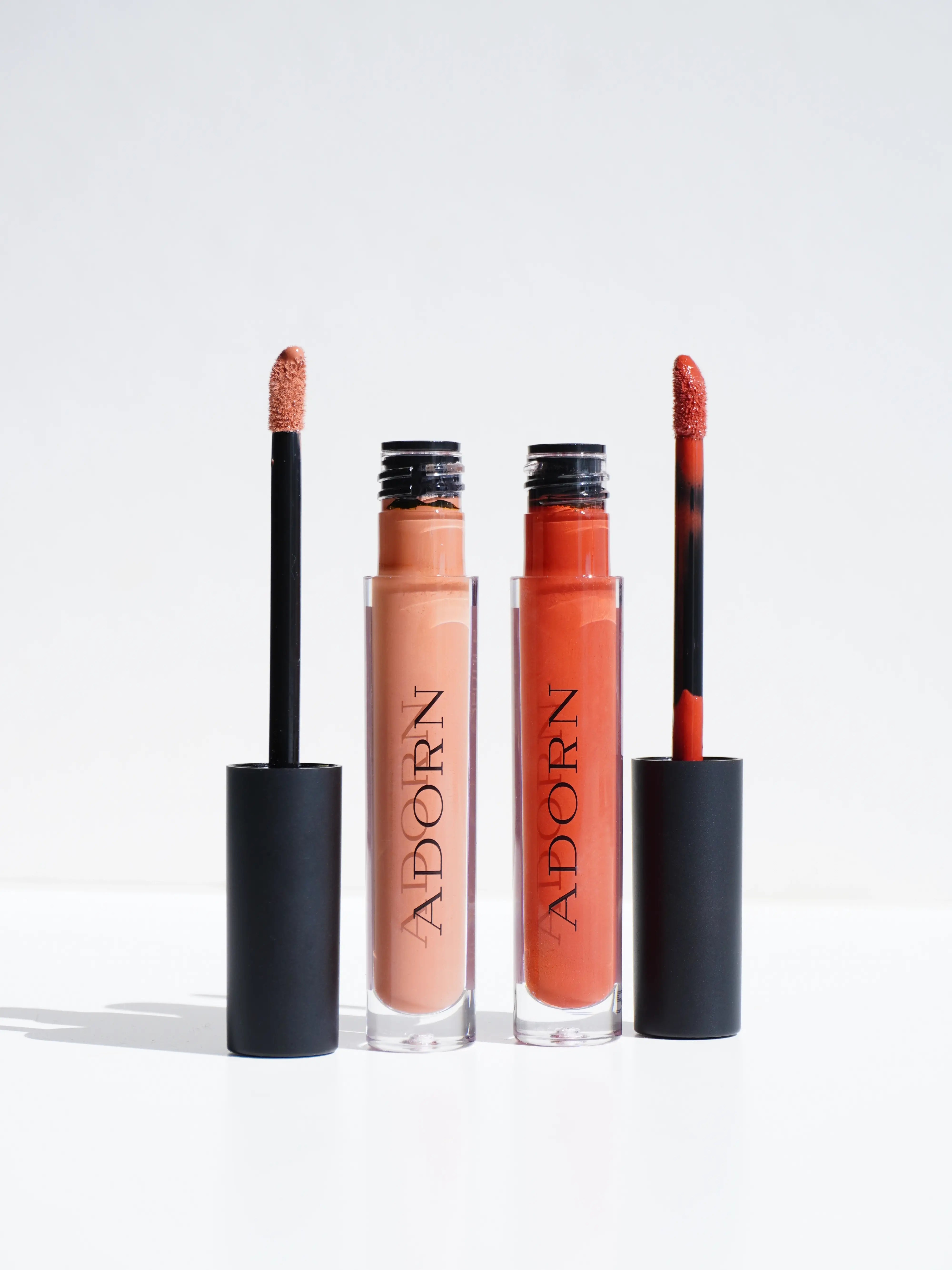 Two lip glosses with applicators on a white background, branded 'Adorn'.