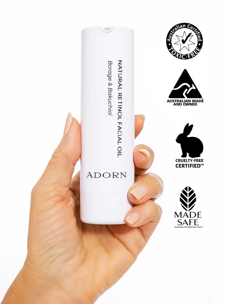 Hand holding a white bottle of 'Adorn' natural retinol facial oil with certification logos on a white background.