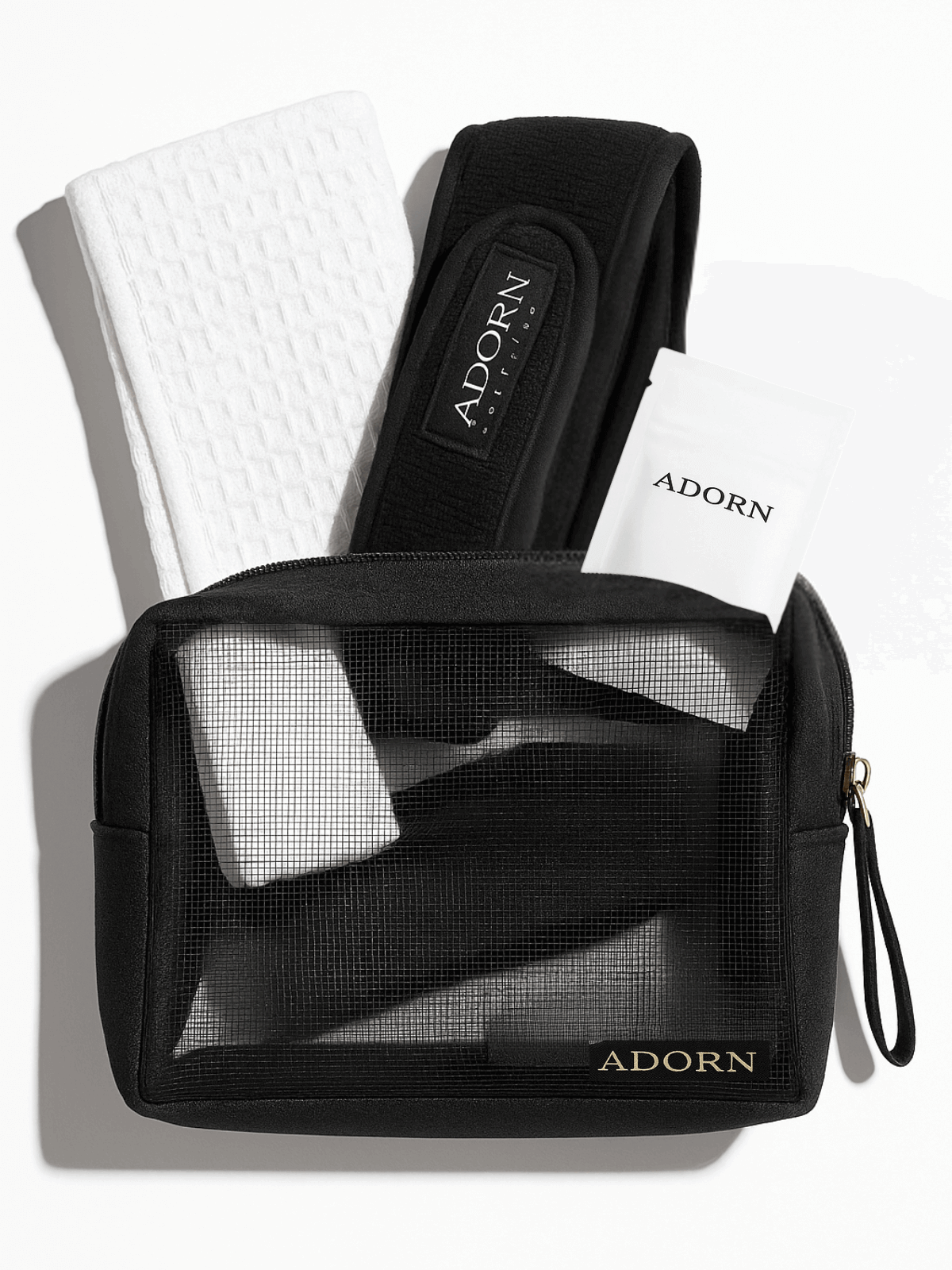 Black toiletry bag with mesh pocket, white towel, and black hairband on a white background with 'ADORN' branding.