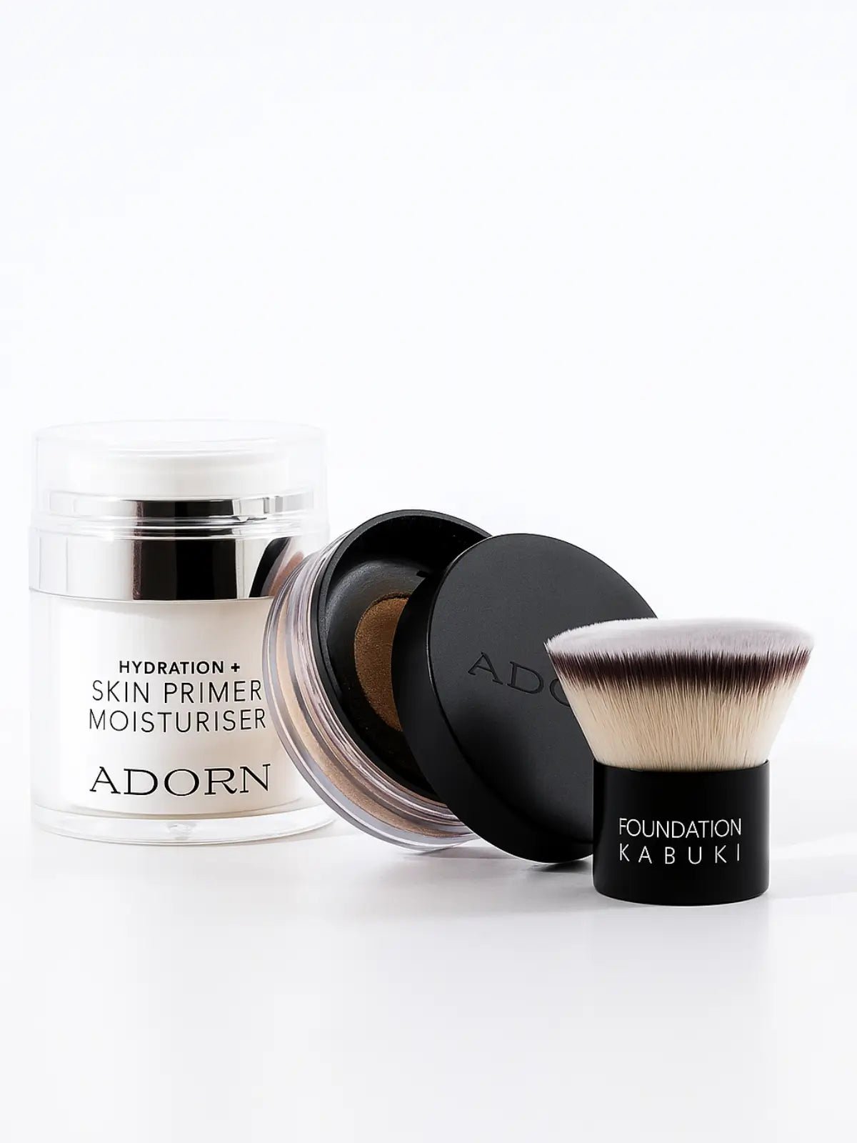 Makeup products including a jar, a black container with a brush, and a white container labeled 'Adorn' on a white background.