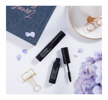 Natural everyday, classic chic Hello Lashes Organic Mascara among a purple bunch of flowers, paperclip, and notebook